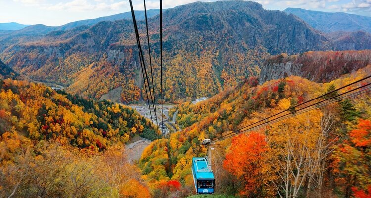 a cable car of Kurodake Ropeway flying over colorful autumn forests on the mountainside in Sounkyo Gorge in Daisetsuzan National Park, in Kamikawa, Hokkaido Japan